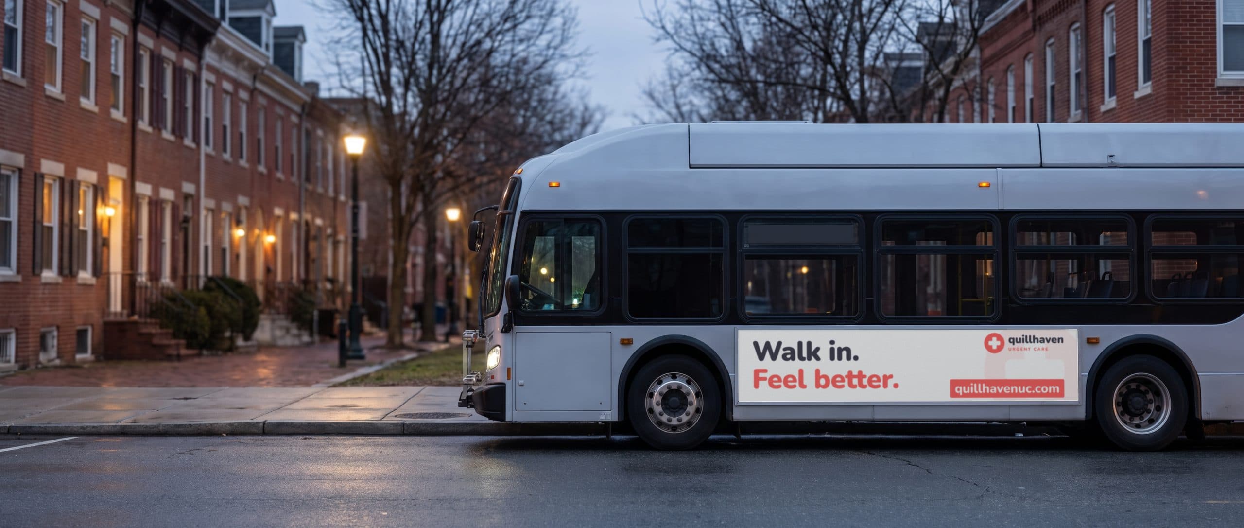 A city bus at dusk on a brick rowhouse street, carrying an urgent care ad along its side.