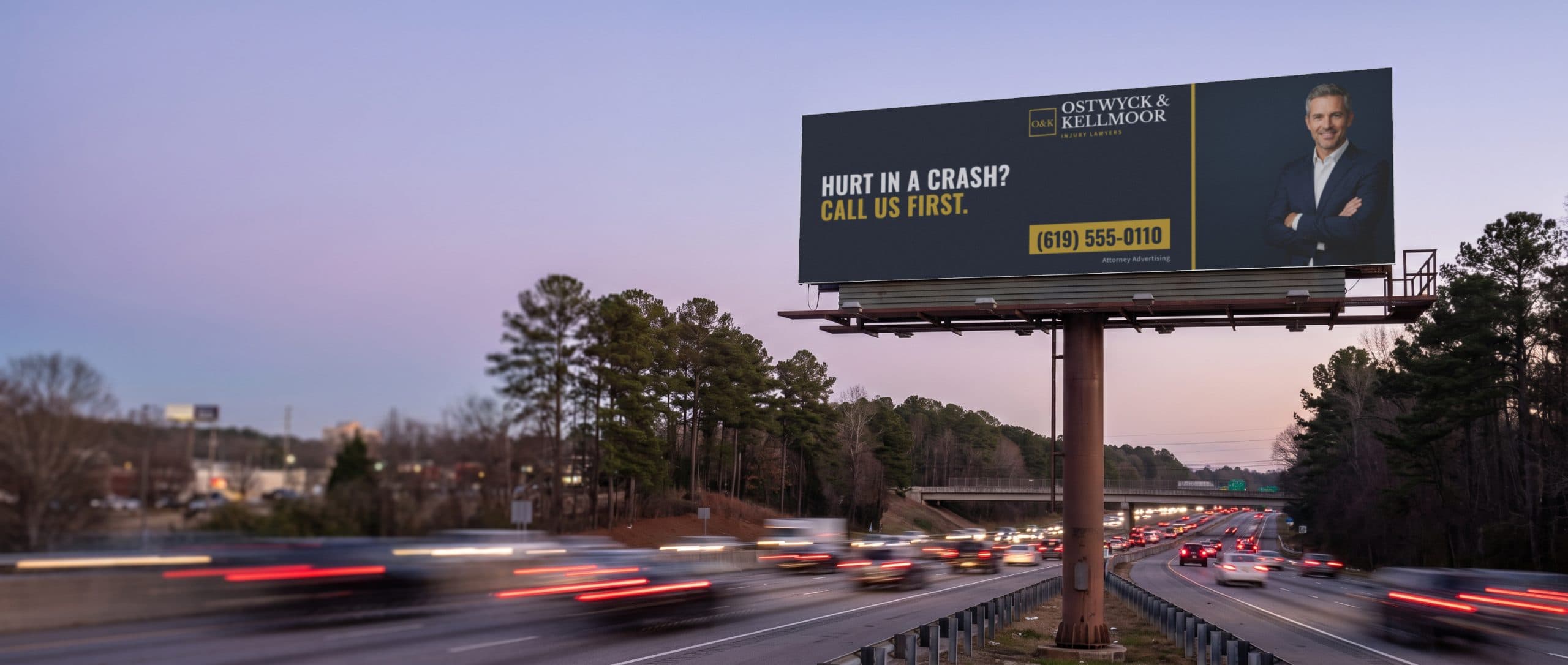 An interstate billboard at dusk above traffic, showing a personal injury law firm ad.