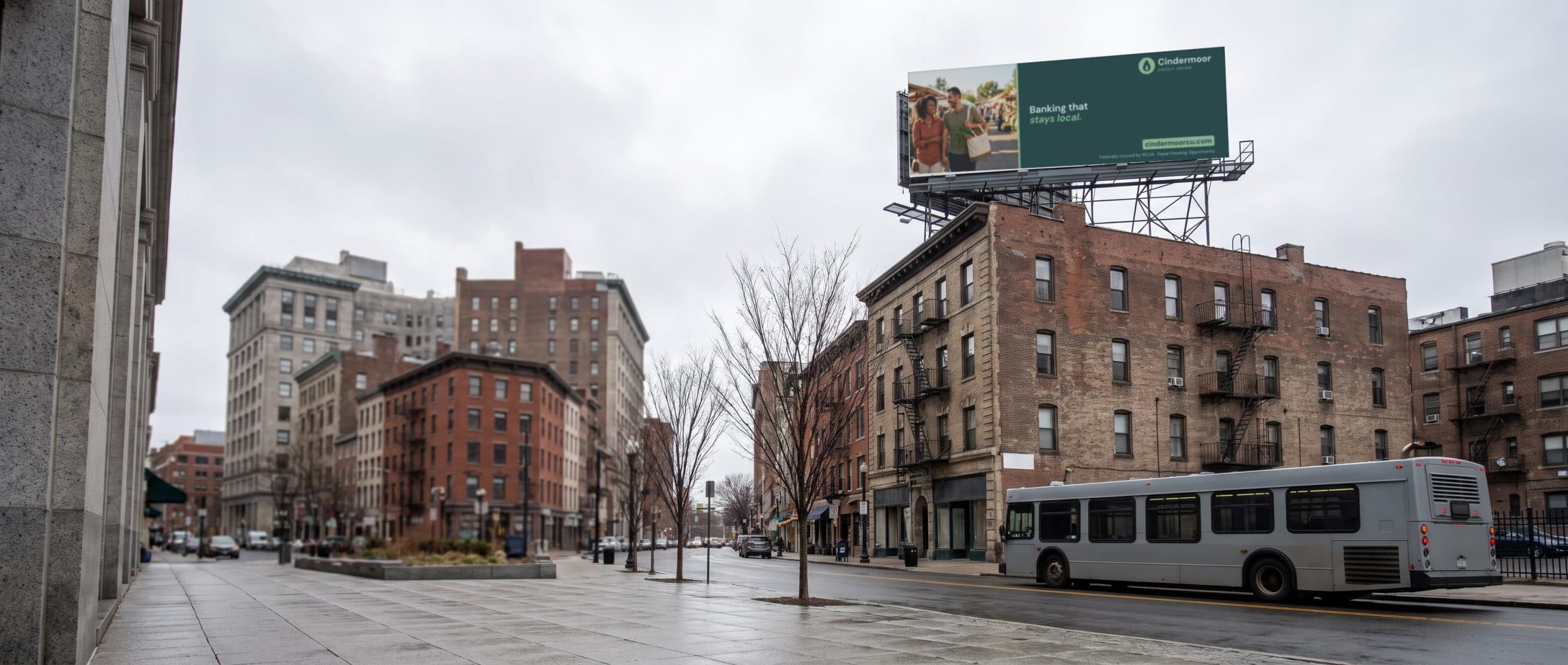 A rooftop billboard above a Northeast city street with a bus passing below, showing a credit union ad.